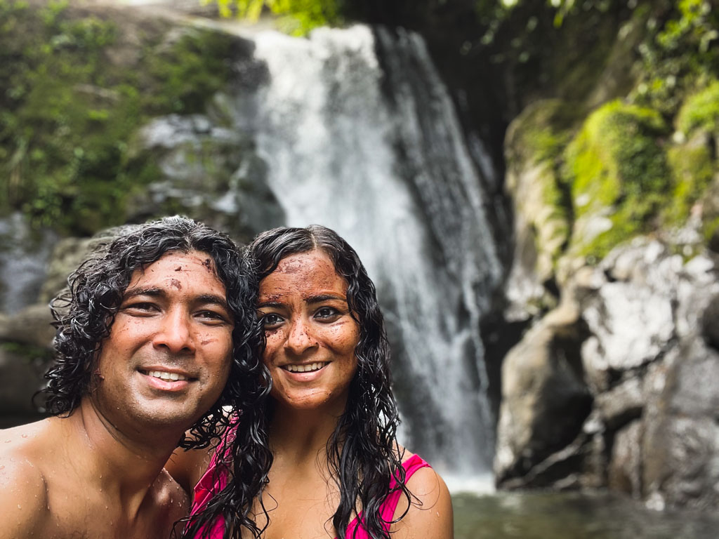 A couple with chocolate masks on their faces, posing for a selfie, in front of the Dos Aguas waterfall around Puerto Viejo de Talamanca in Costa Rica.