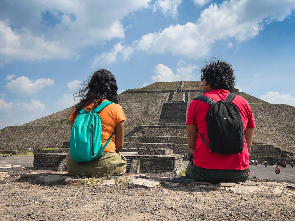 Backside photo of a couple seated on a platform with view of the Pyramid of the Sun at the Teotihuacan archaeological site, a nice day trip from Mexico City.