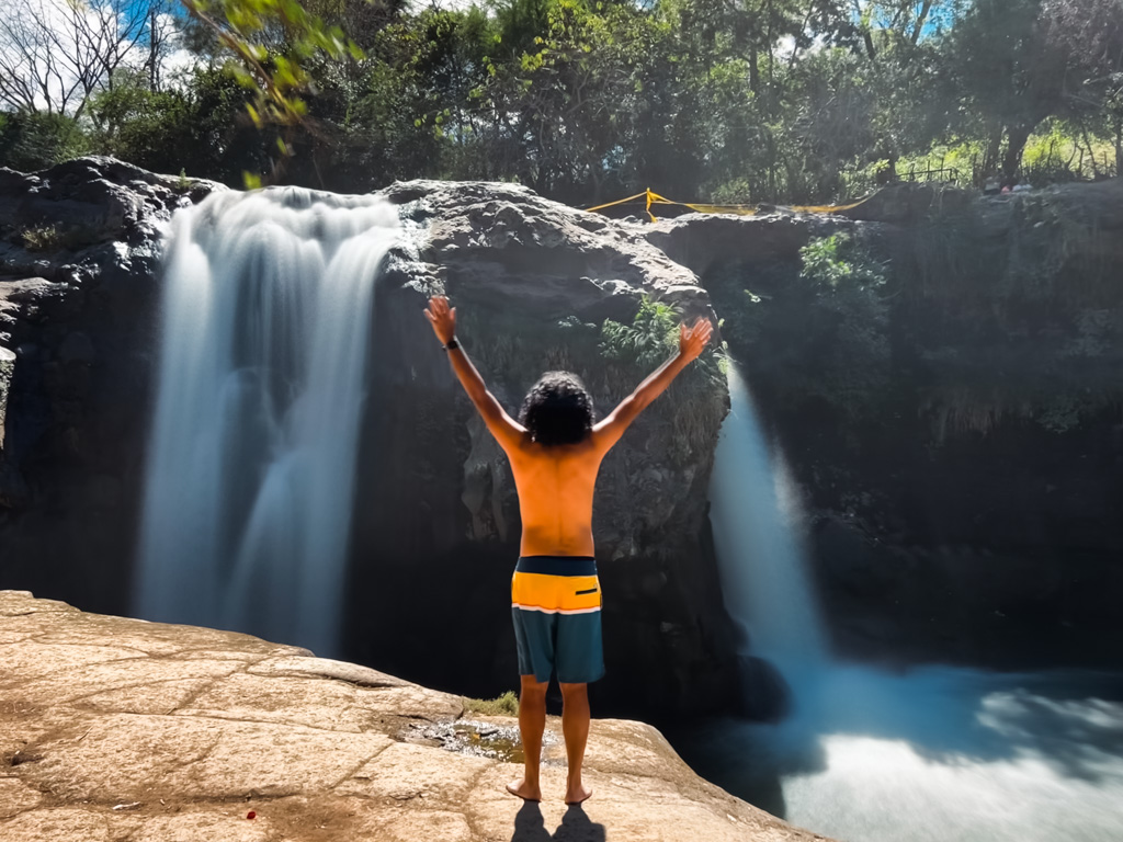A man in blue and yellow shorts, standing on the edge of the cliff, waiting to jump into the waterfall pool of El Salto.