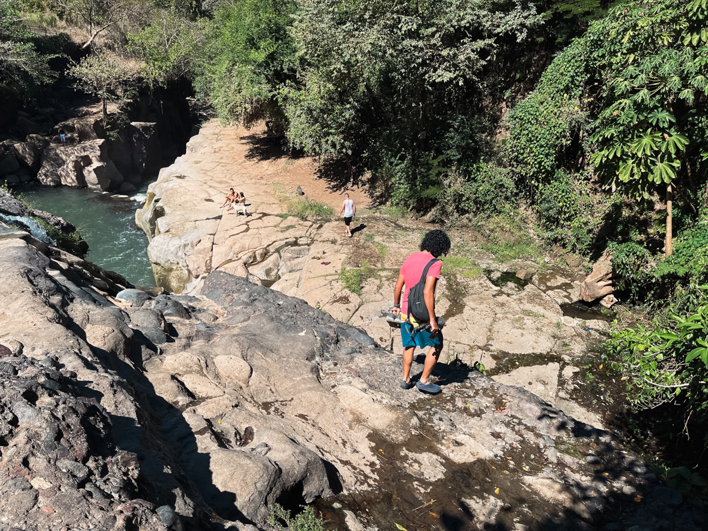 A man navigating the tricky trails at El Salto, and a couple of people are seated on a rock in the distance.