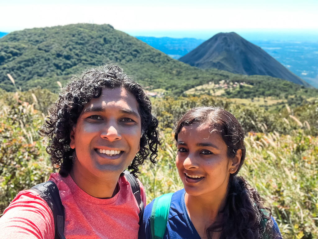 Selfie of a couple on the Santa Ana volcano hike trail, with the Cerro Verde volcano and the Izalco volcano in the backdrop.