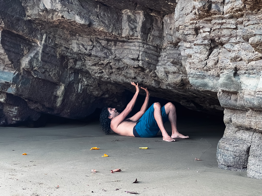 A man lying on the ground, posing to push against the cave at the beach.