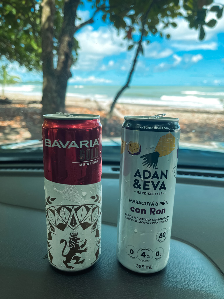 Couple of chilled beverages placed on the dashboard inside a car, while the view looks out to the Pacific Ocean.