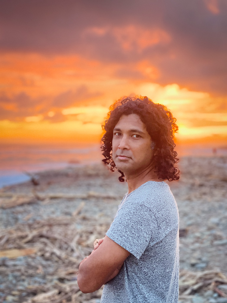 A man standing at Dominical beach, against the backdrop of a fiery sunset sky.
