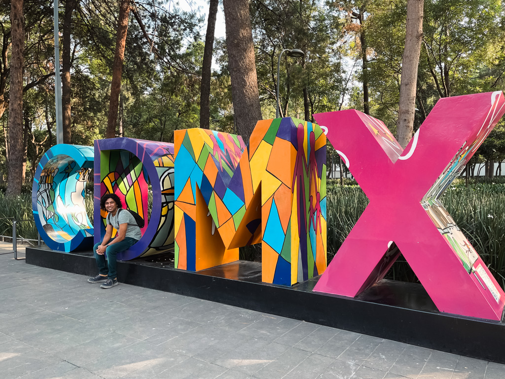 A man seated on the base of a CDMX sign in Mexico City.