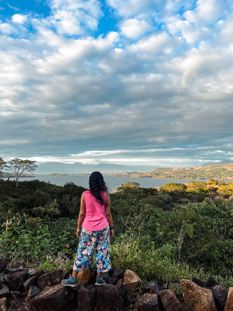 The backside view of a woman standing on a rock, enjoying the view of Lake Suchitlan, from the viewpoint at Cascasa Los Tercios in Suchitoto, El Salvador.