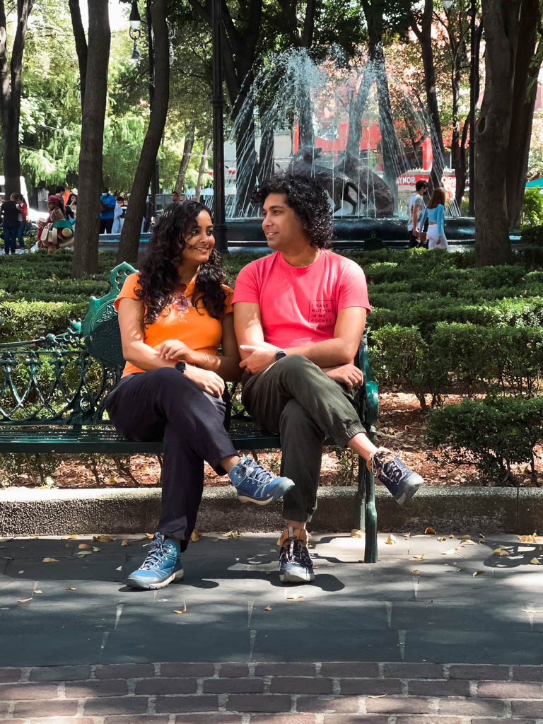 A man and a woman sitting on a public bench in a Plaza in Coyoacan, Mexico City.