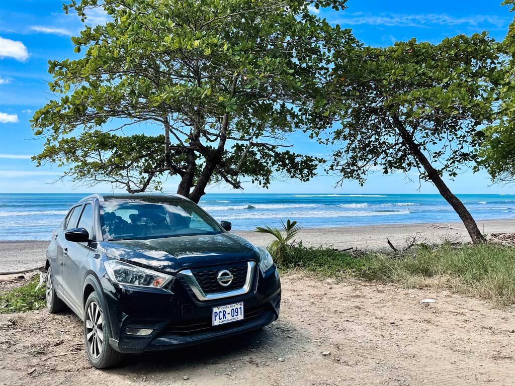 A black car parked next to the beach, with blue Pacific Ocean in the backdrop. Nicoya Peninsula of Costa Rica.