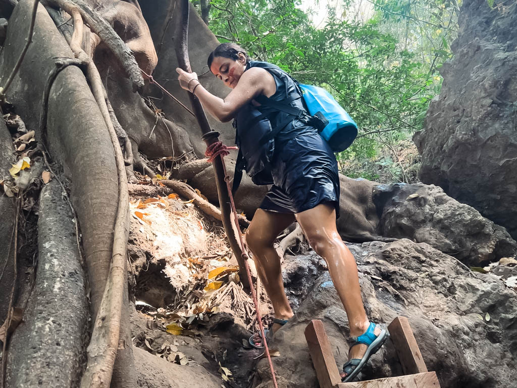 A woman climbing down a ladder during a hike in the La Leona waterfall trail. She is carrying a dry bag, a packing essential for Costa Rica in the rainy season