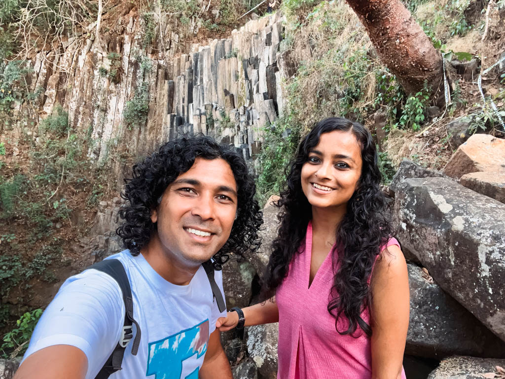 A couple posing for a selfie at Los Tercios waterfall, one of the top things to do in Suchitoto. There is no water but the unique waterfall wall behind is visible in the background.