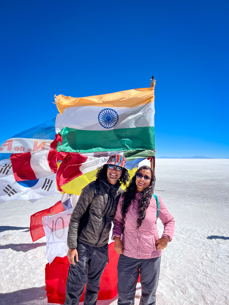 Couple standing in front of Indian flag in Salar de Uyuni of Bolivia. Flags of other countries in the background.