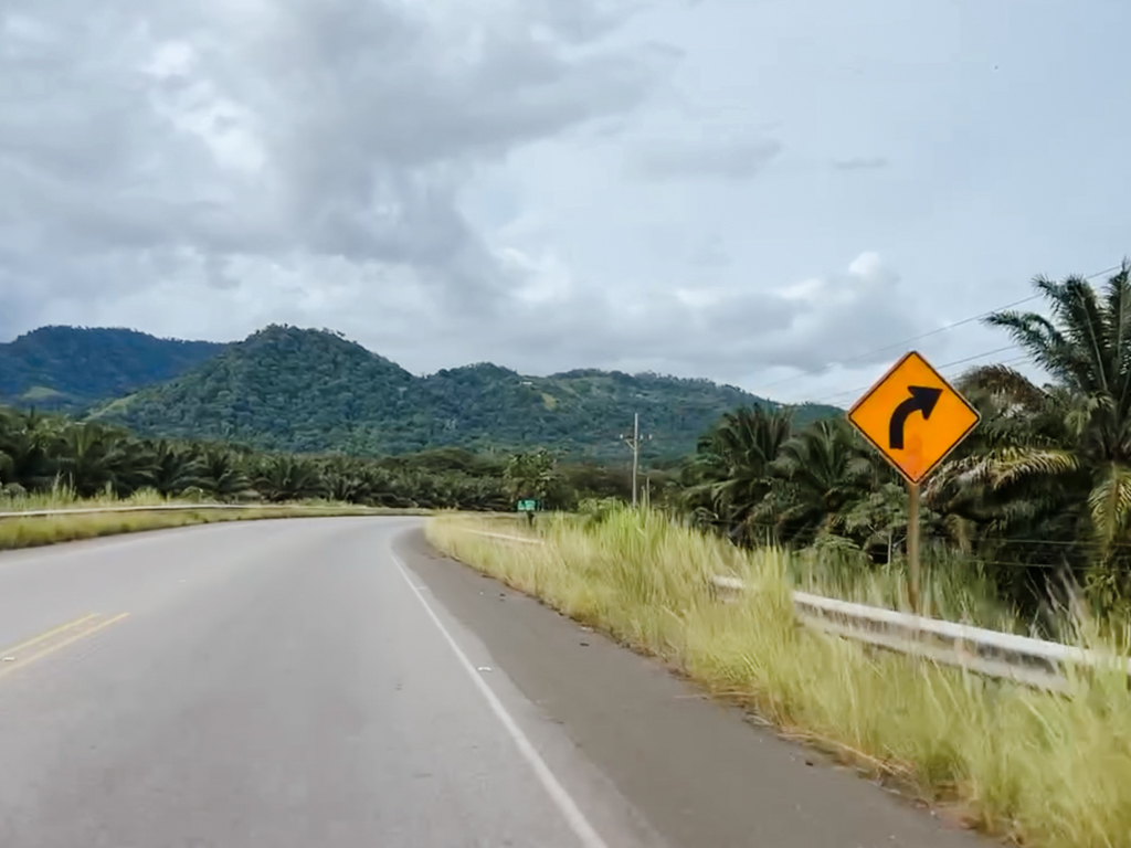 Road to Manuel Antonio, on the Pacific coast of Costa Rica, with views of green hills and road signs on a cloudy day.