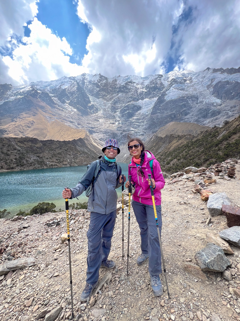 A man and a woman standing in front of the Humantay Lake and Snow-capped mountains in Peru, with trekking poles in hand.