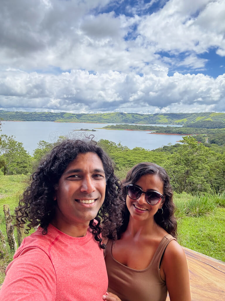 A man and a woman smiling with the Lake Arenal visible behind them, on the way from La Fortuna to Monteverde.