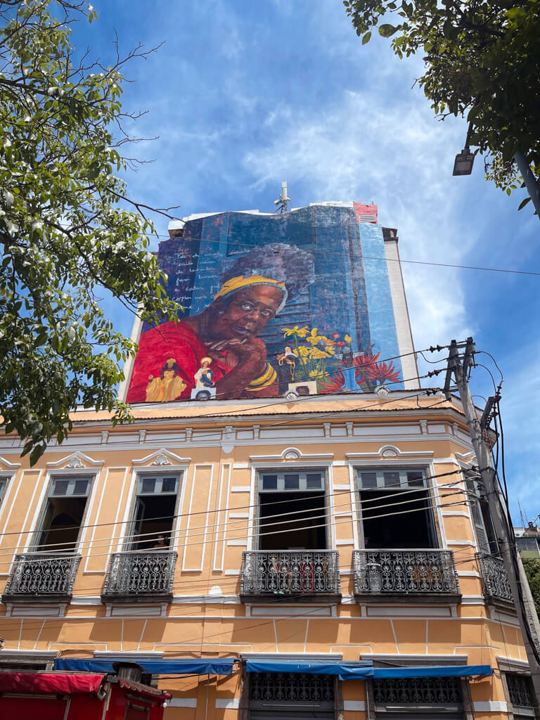 A big wall mural on a large wall in the background of a building with balconies. A sight in Little Africa in Rio de Janeiro.