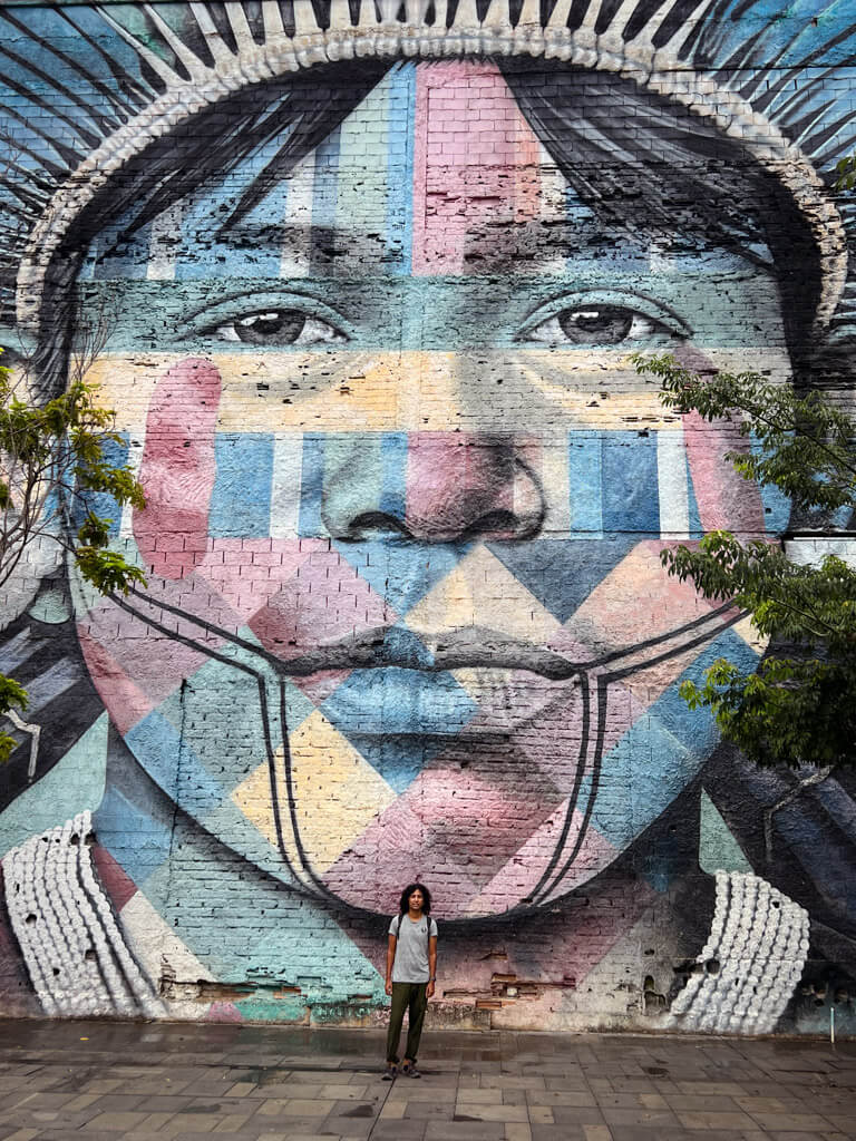 Man standing against the wall of Mural das Etnias and looking tiny in comparison.