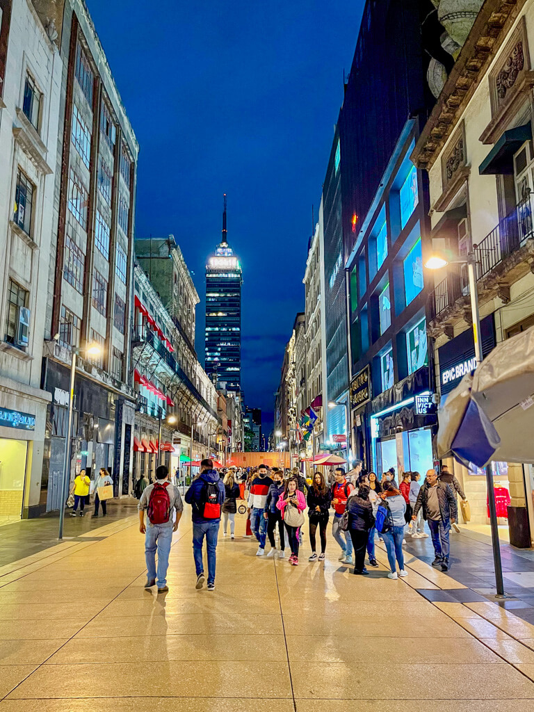 People walking on a street in Zocalo, Mexico City, at night.