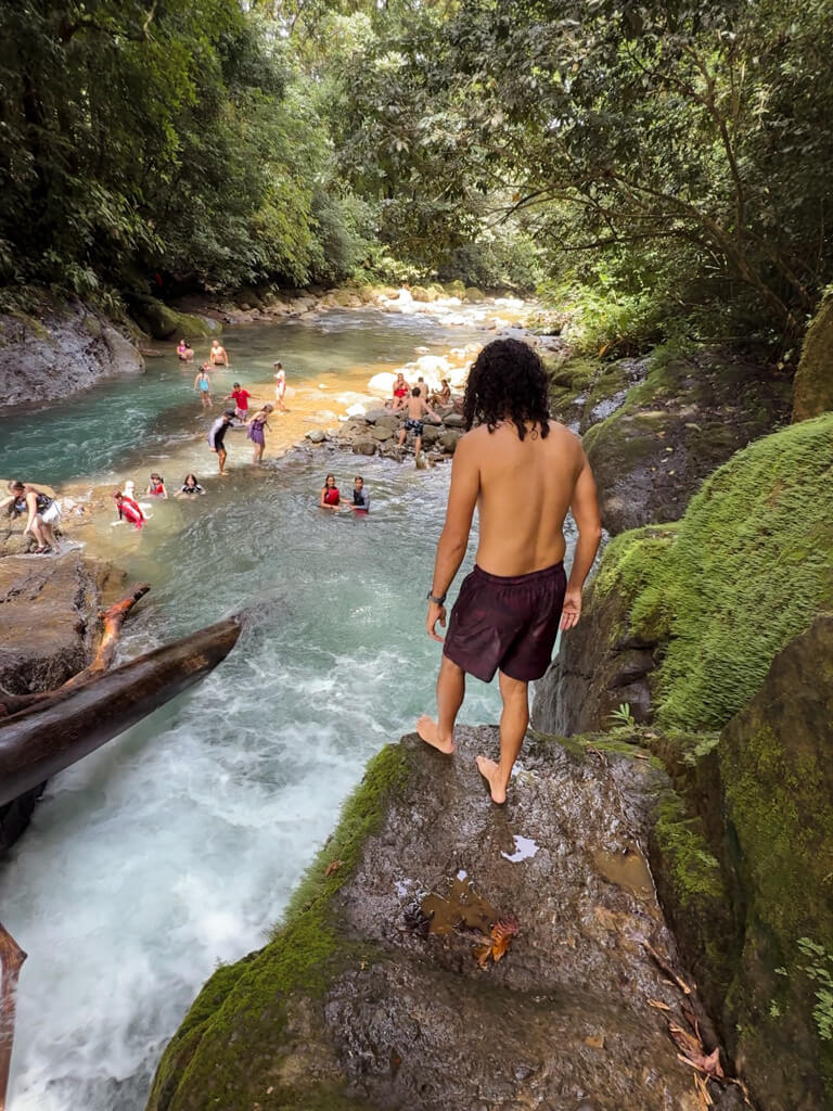 A man standing on the ledge of a rock, moments before attempting a waterfall jump in Costa Rica.