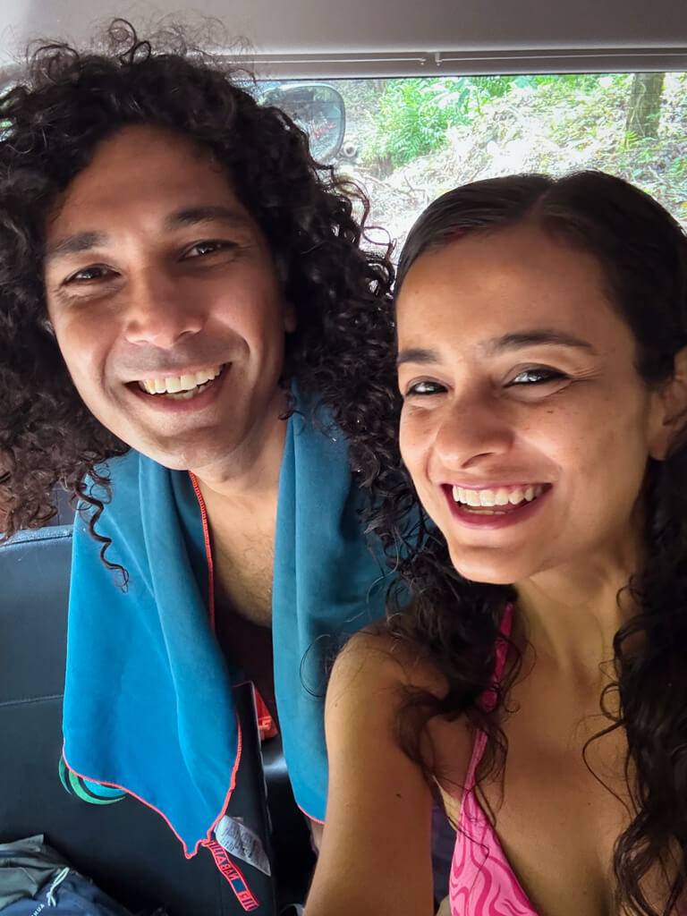 A man and a woman, ready for a swim, taking a selfie inside a vehicle.