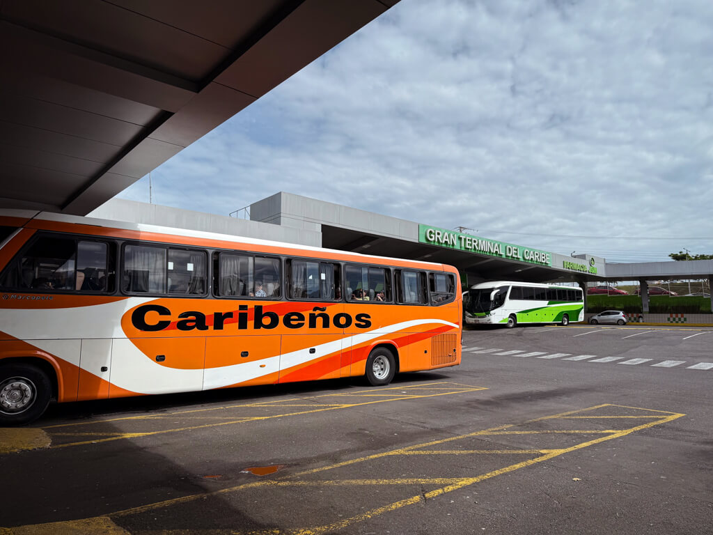 An orange colored bus with Caribeños written on it, standing at Gran Terminal del Caribe in San Jose. Another green and white bus can be seen at the back.