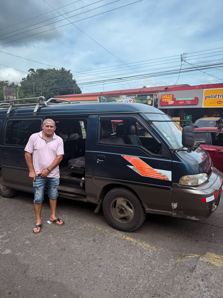 A man in pink t-shirt and jeans capris, standing next to the shared taxi from Pavona to Tortuguero.