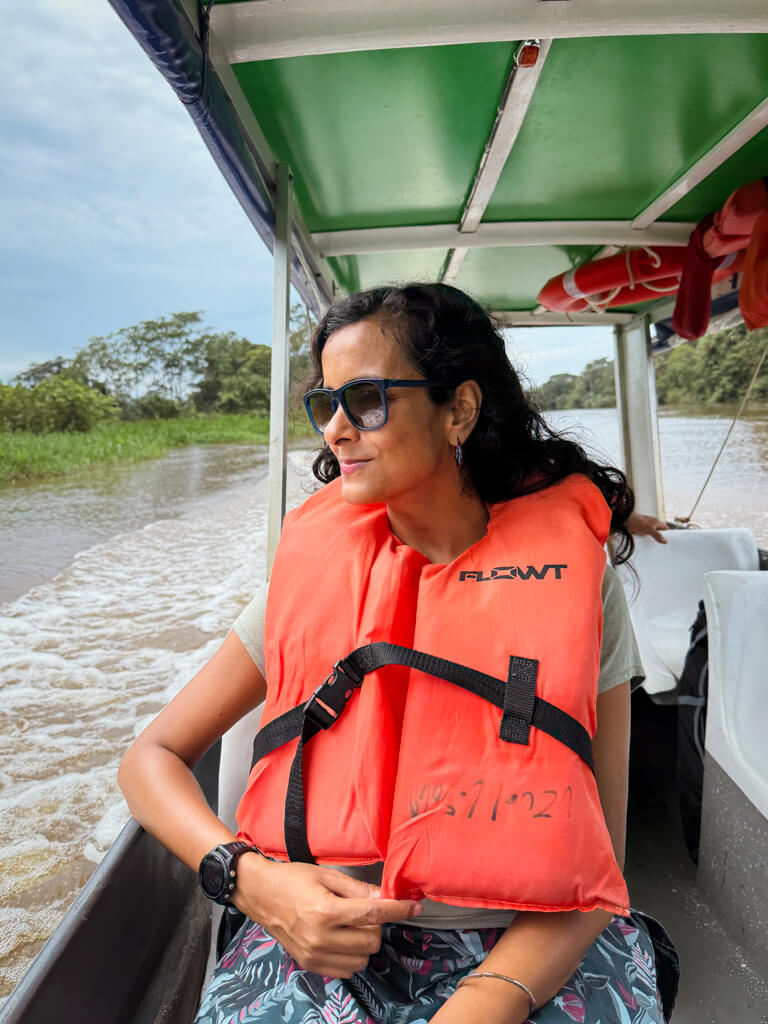 A woman, with life jacket on, seated in a boat from Pavona to Tortuguero, and smiling while enjoying the scenery.