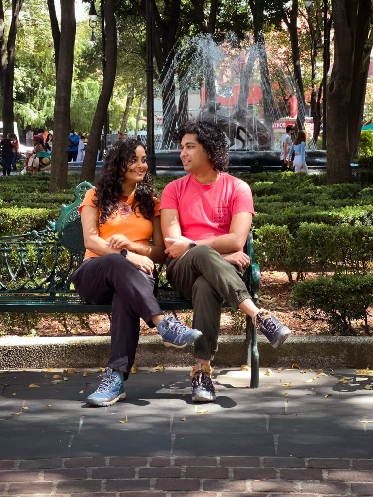 A man and a woman, seated on a park bench at Parque Centenario in Coyoacan, Mexico City.