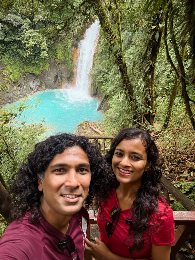 A man and a woman posing for a selfie with Rio Celeste waterfall in the background.