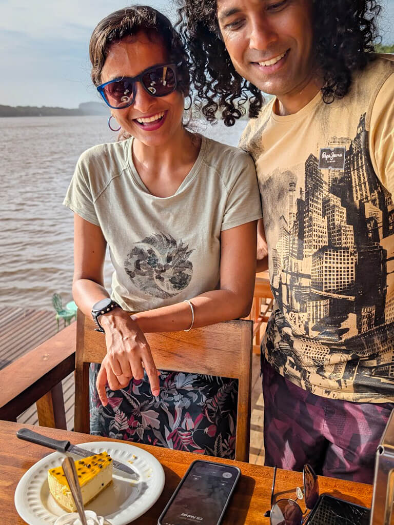 A man and a woman standing at a riverside restaurant, with a cake in front on the table, for birthday celebration.