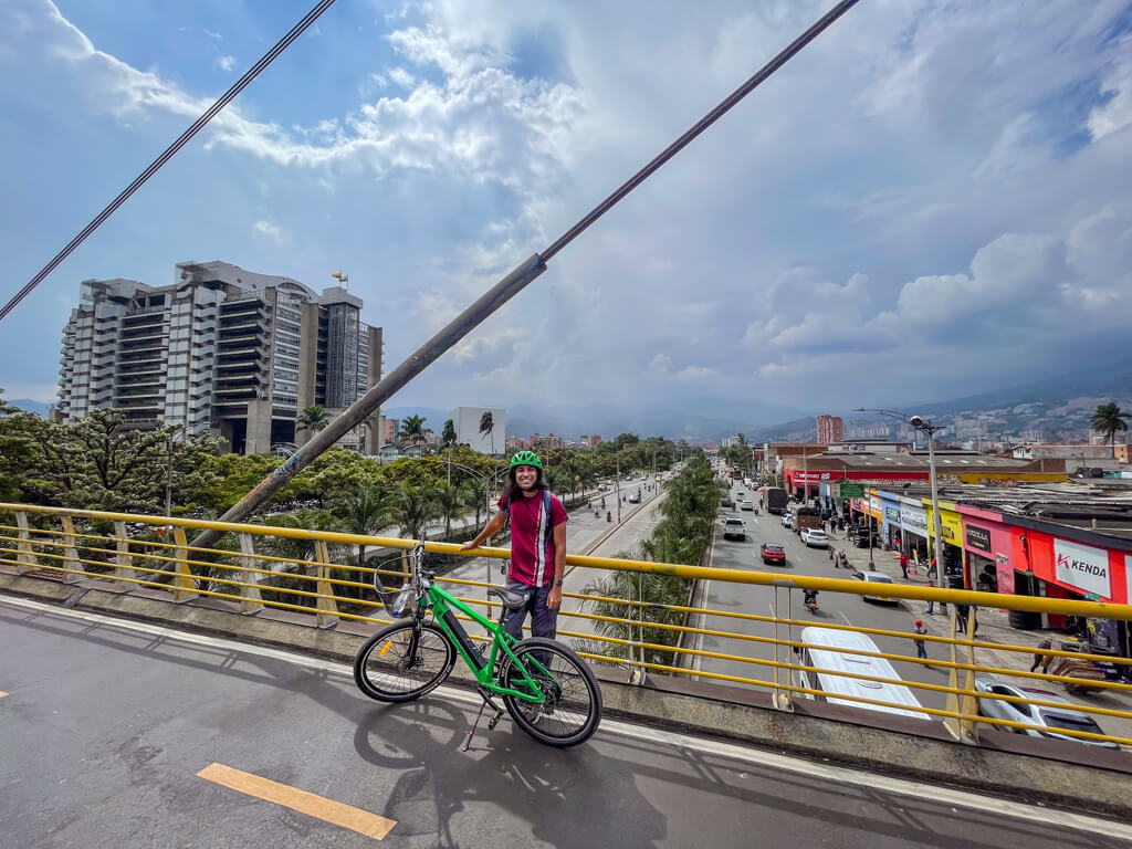 A man standing with a green colored electric bike on a bridge over roads of Medellin near the center of the city during a Medellin Bike Tour.