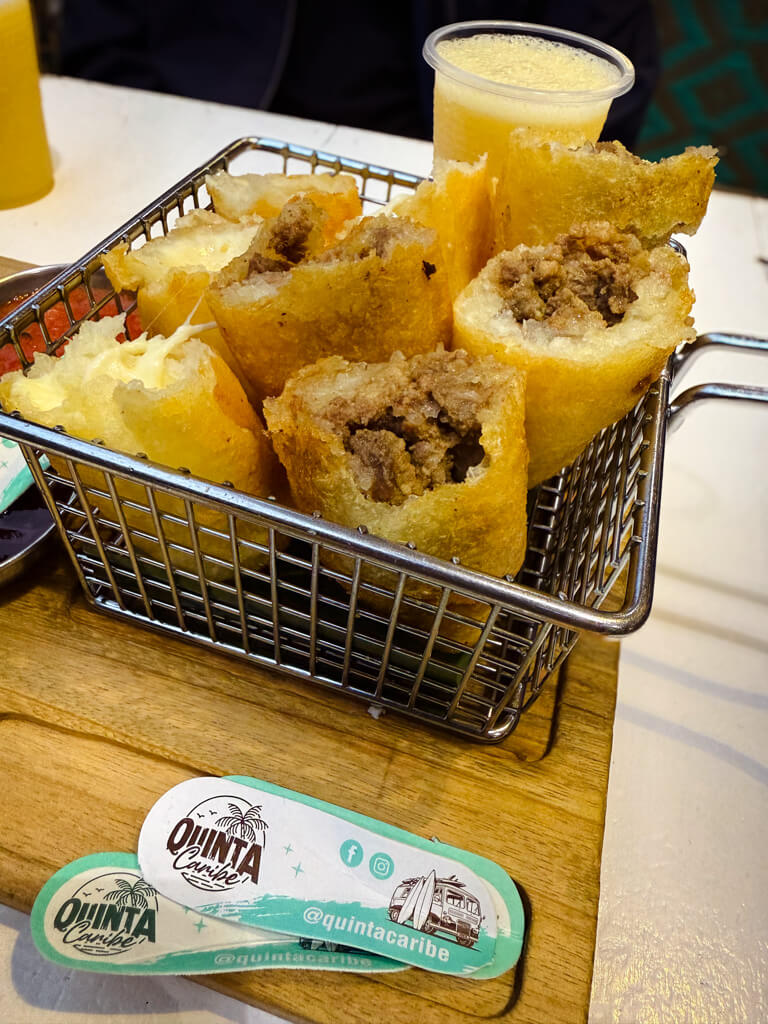 A basket of meat and cheese carimañolas, with a glass of guava juice on the side.