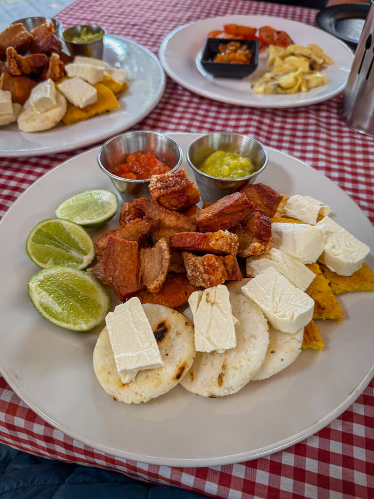 A plate full of Chicharron, Chorizo, Arepas, Queso, Guacamole, Hogao.