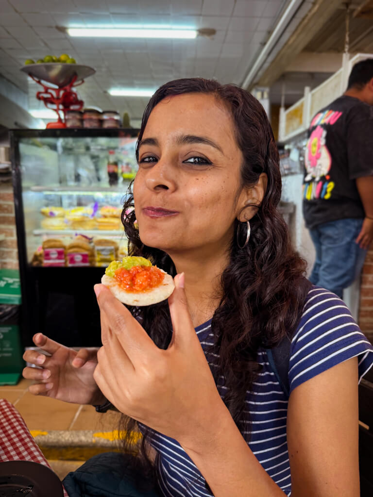 A woman holding an arepa topped with guacamole and hogao.