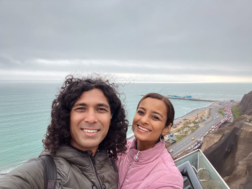 A man and woman with the coastal road of Lima and Pacific ocean in the background.