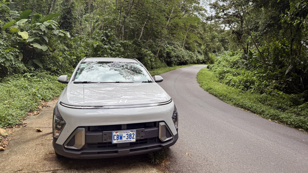 A Hyundai Kona rental car from Adobe Rent A Car, parked by the roadside, with lush forest on either side, on a road trip in Costa Rica.