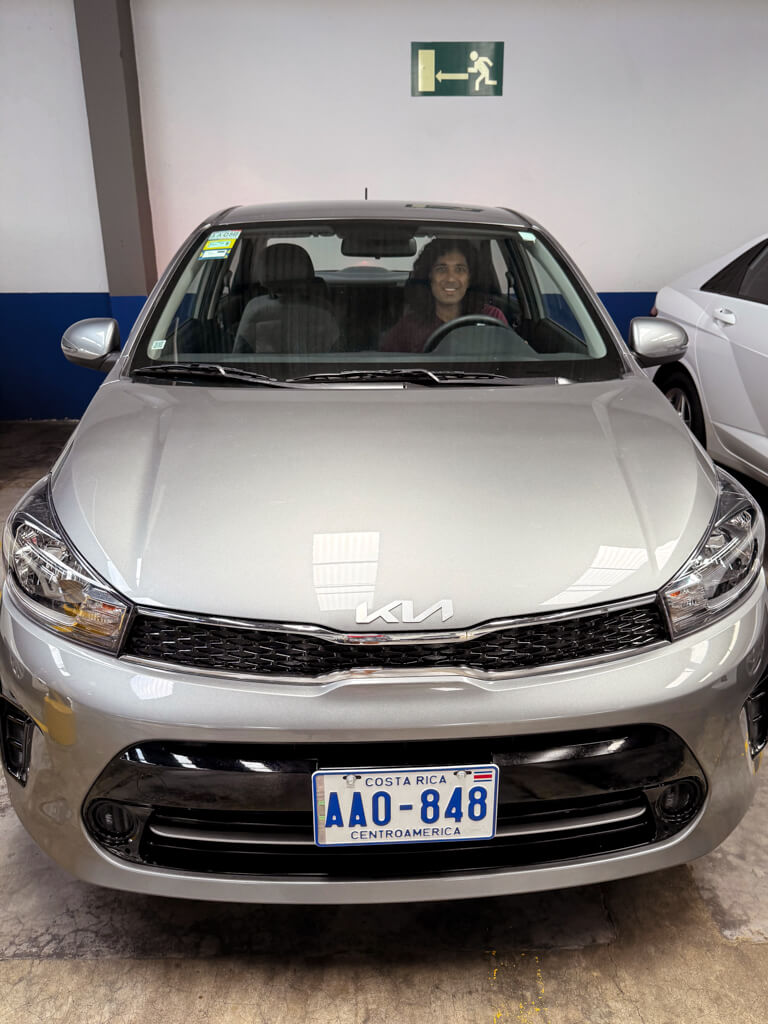 A man in the driver's seat of a Kia Soluto, a rental car, when renting a car from Adobe at San Jose Airport office.