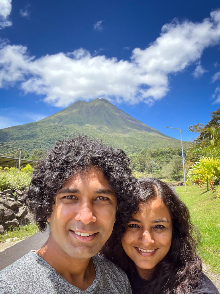 Spectacular reveal of the Arenal Volcano in the backdrop of a man and a woman posing for a selfie. Los Lagos Hotel Spa & Resort review.