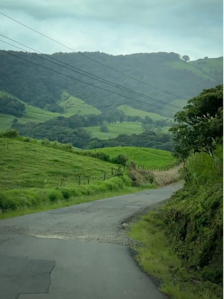 Costa Rica road with a mix of paved and unpaved sections, with views of green hills and farmlands.