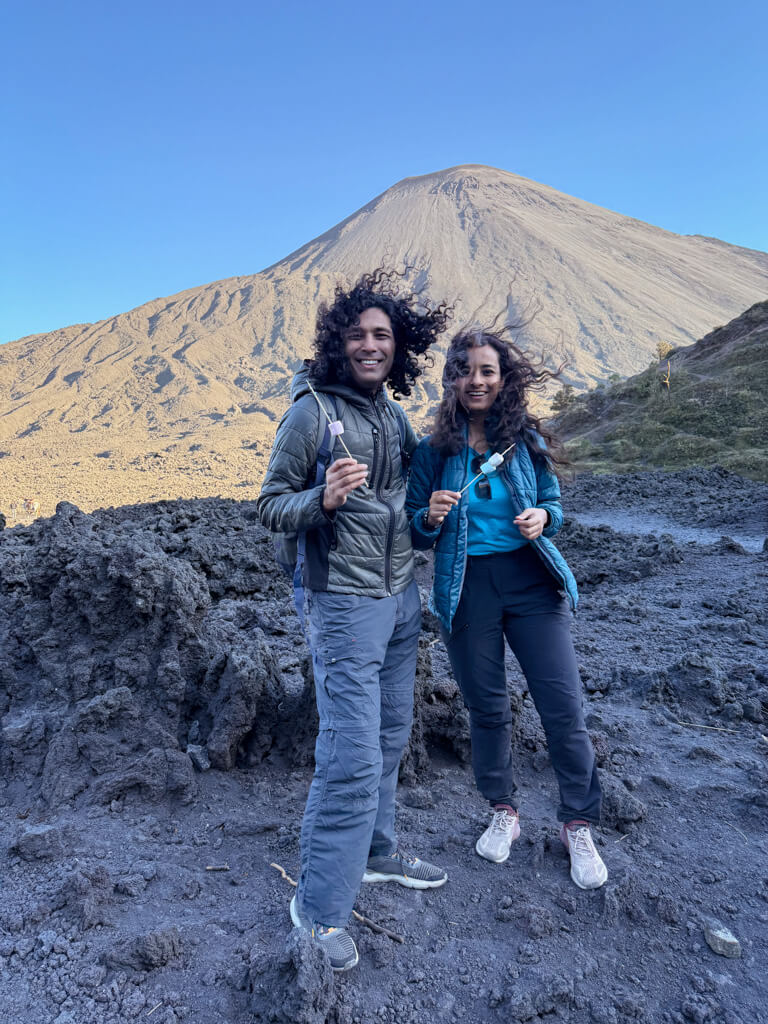 A man and woman standing with marshmallows at the lava field of the Pacaya Volcano.