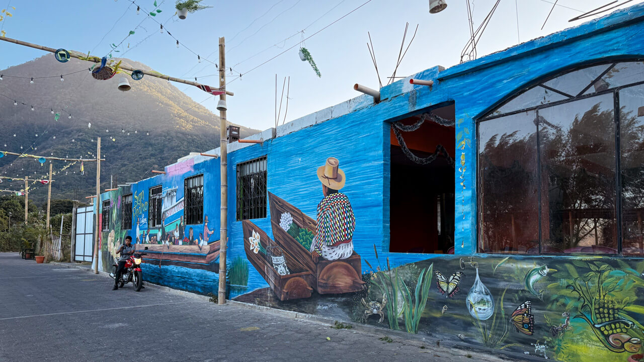 San Pedro La Laguna town with a colorful mural on one side of the road and the view of San Pedro Volcano in the distance.