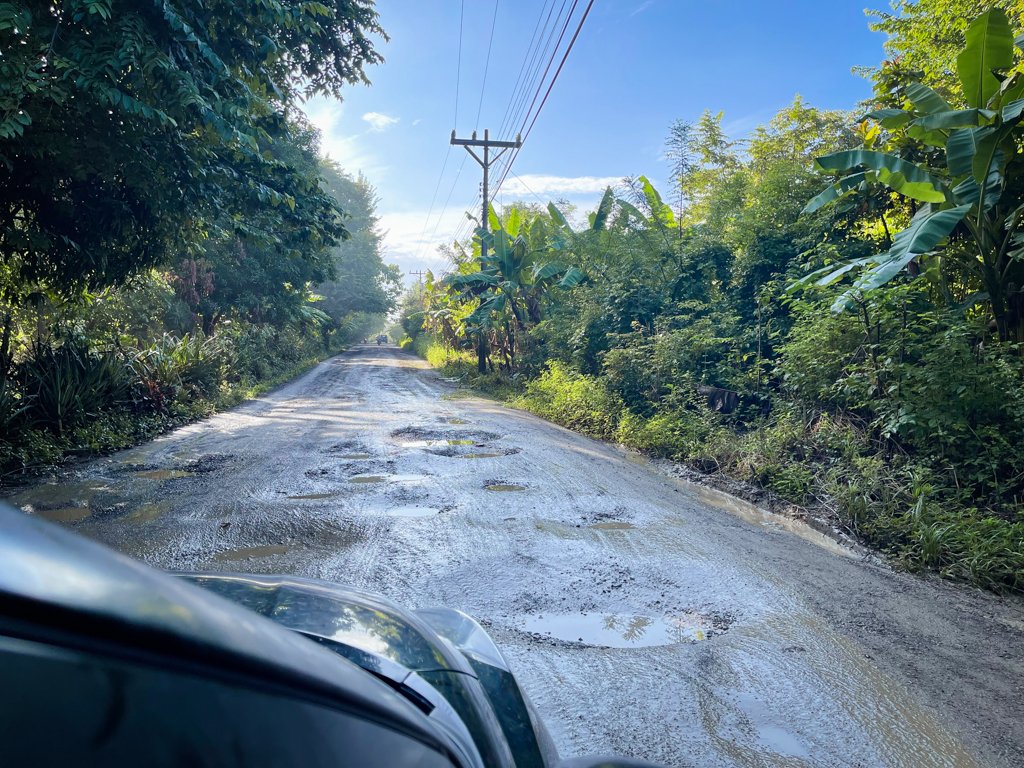 A rural unpaved road in Costa Rica, with potholes filled with rain water.